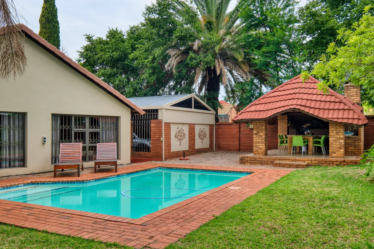 A backyard pool with a brick deck and a tiled gazebo